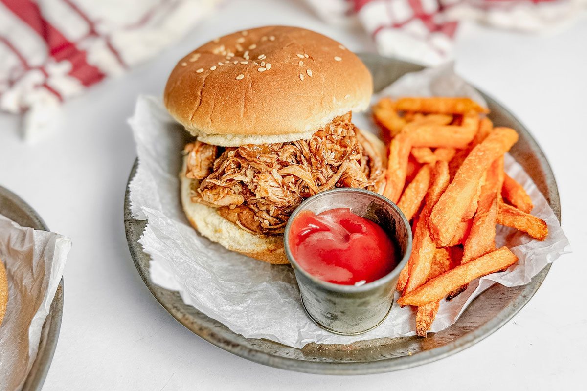 Taste of Home Dutch oven pulled pork on a metal plate with sweet potato fries and tin of ketchup on a marble surface