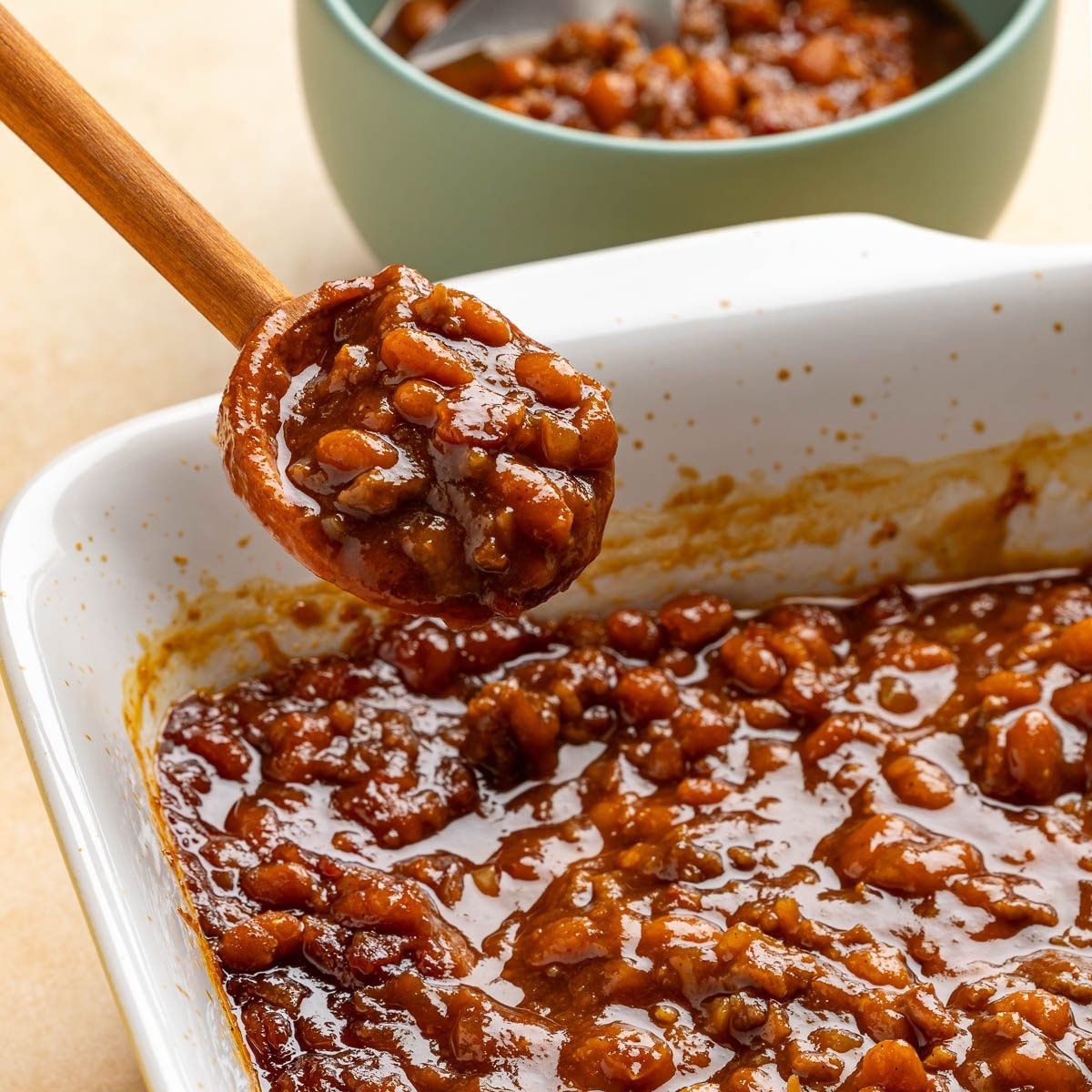 Taste of Home BBQ baked beans recipe photo of a wooden spoon scooping out some bbq baked beans from the baking dish.