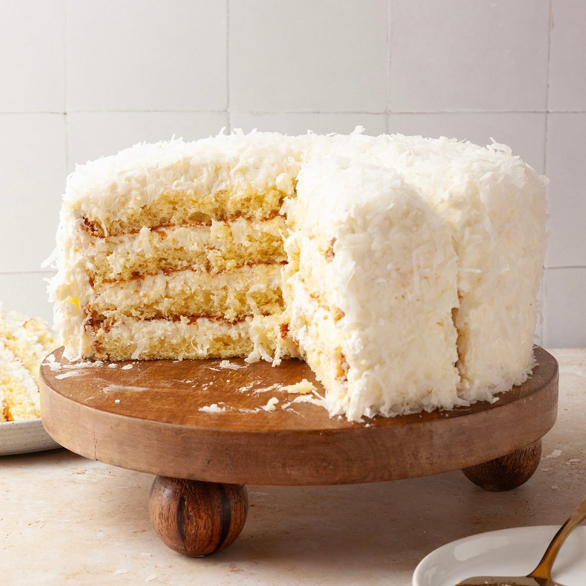 Taste of Home Pineapple Coconut Cake on a wooden platter, slices out, stack of plates