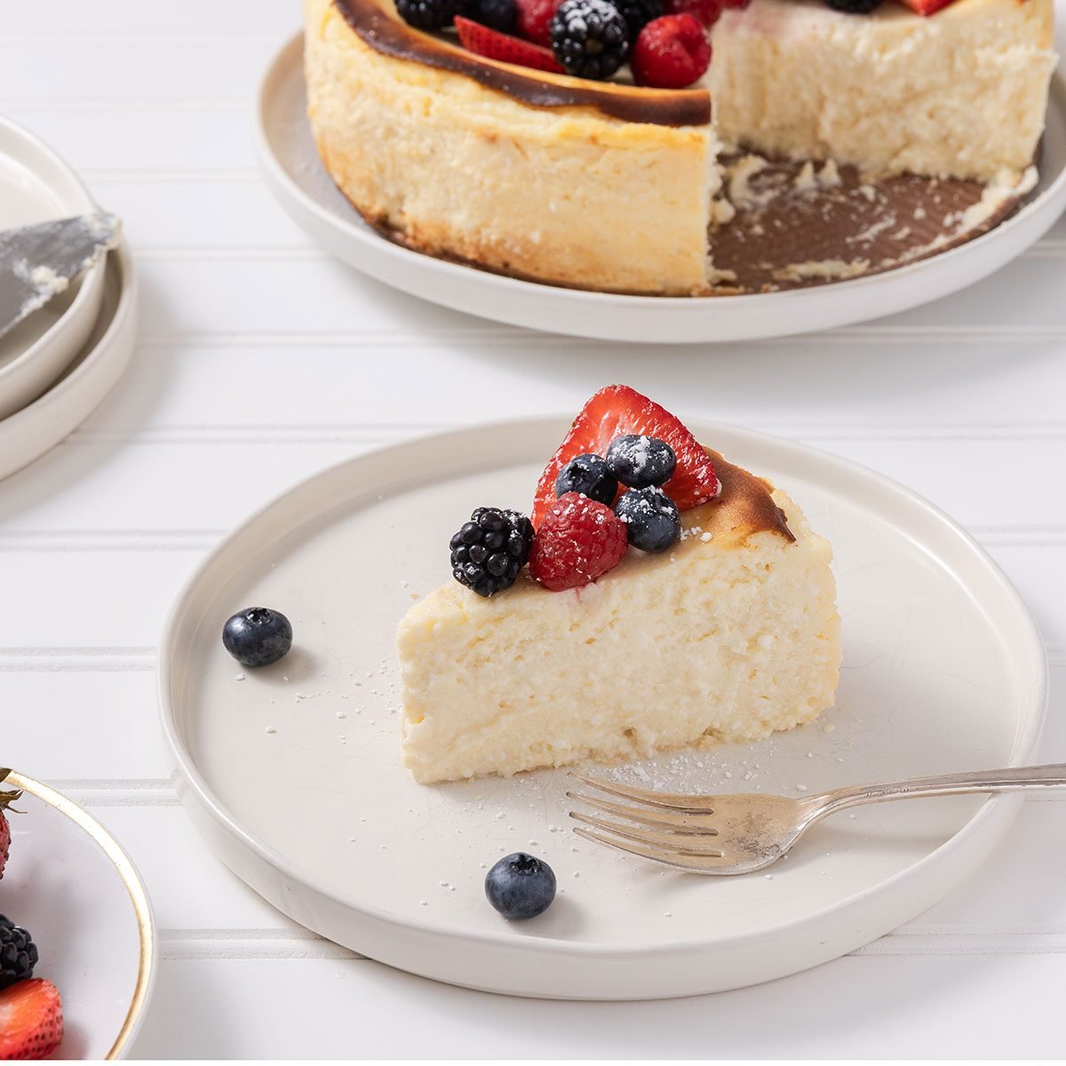 Slice of cheesecake served on plate with full cheesecake in the background.