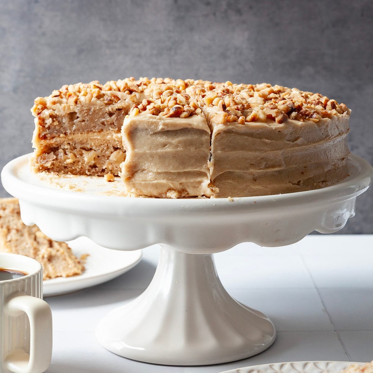 Full yield of Taste of Home Apple Spice Cake on a white cake stand, white serving plates; dessert