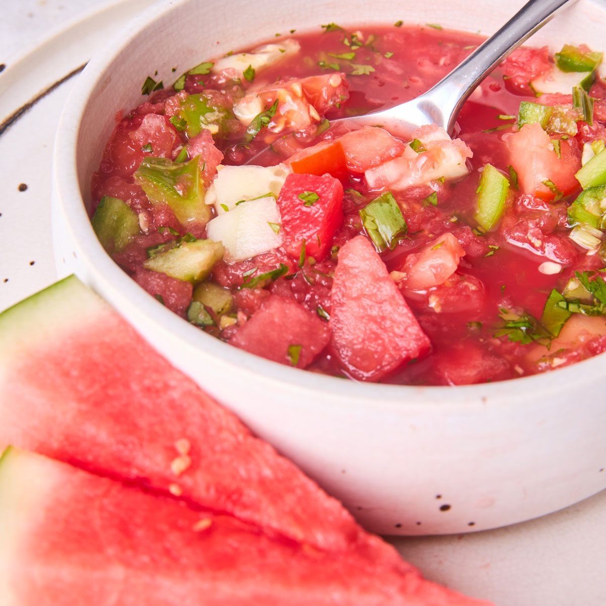 Close up of watermelon gazpacho in bowl with watermelon wedges on plate