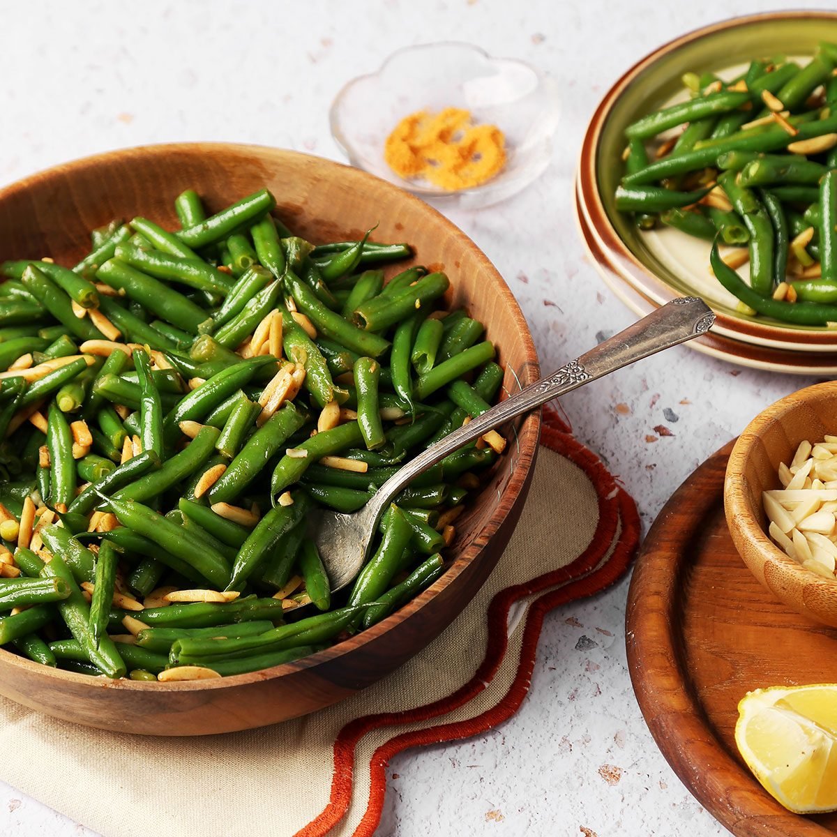 Close up of Taste of Home's Green Bean Almondine served in a wooden bowl on a white surface.