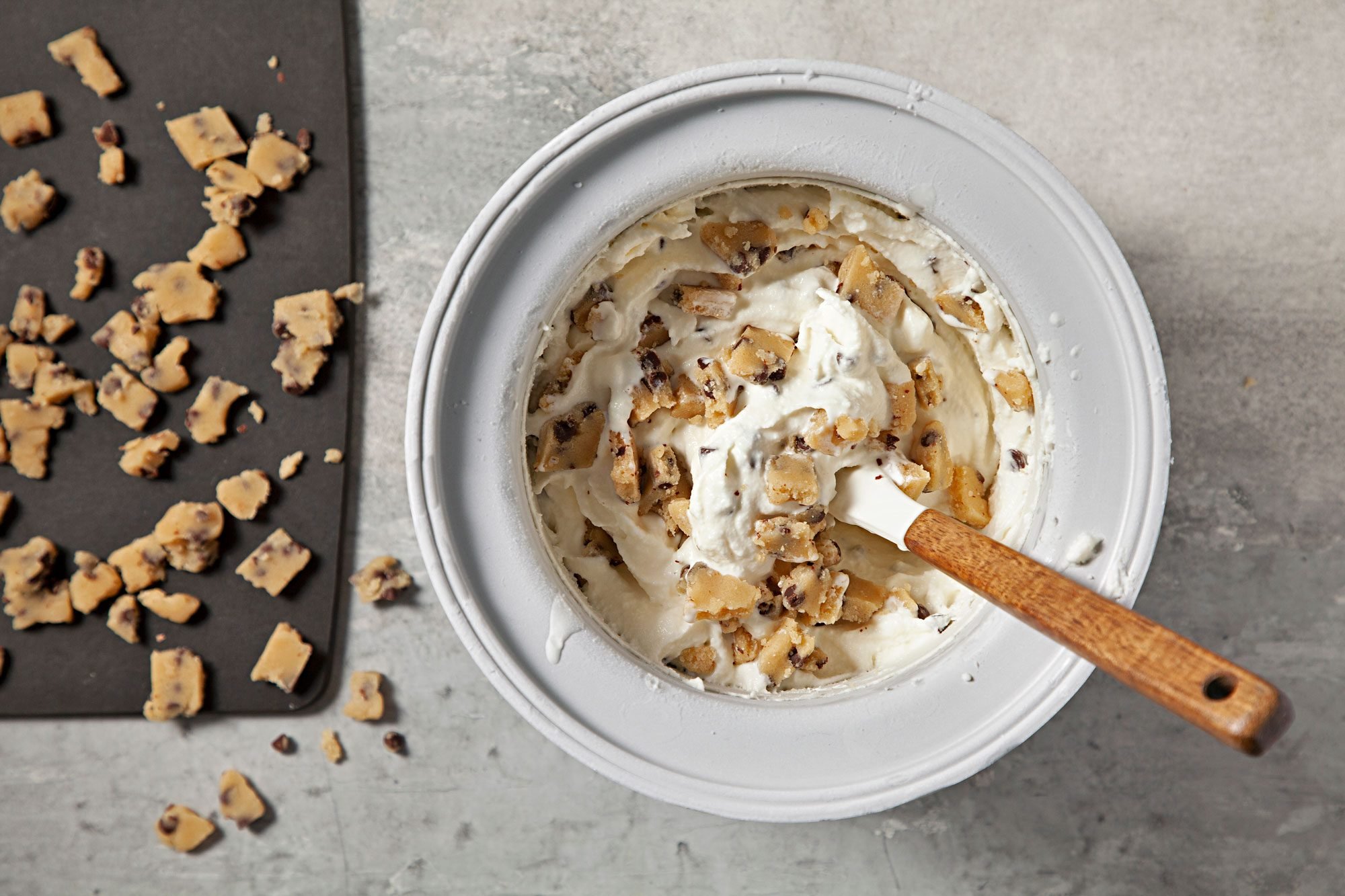 overhead shot; grey background; Chopped cookie dough into small pieces; stiring into ice cream;