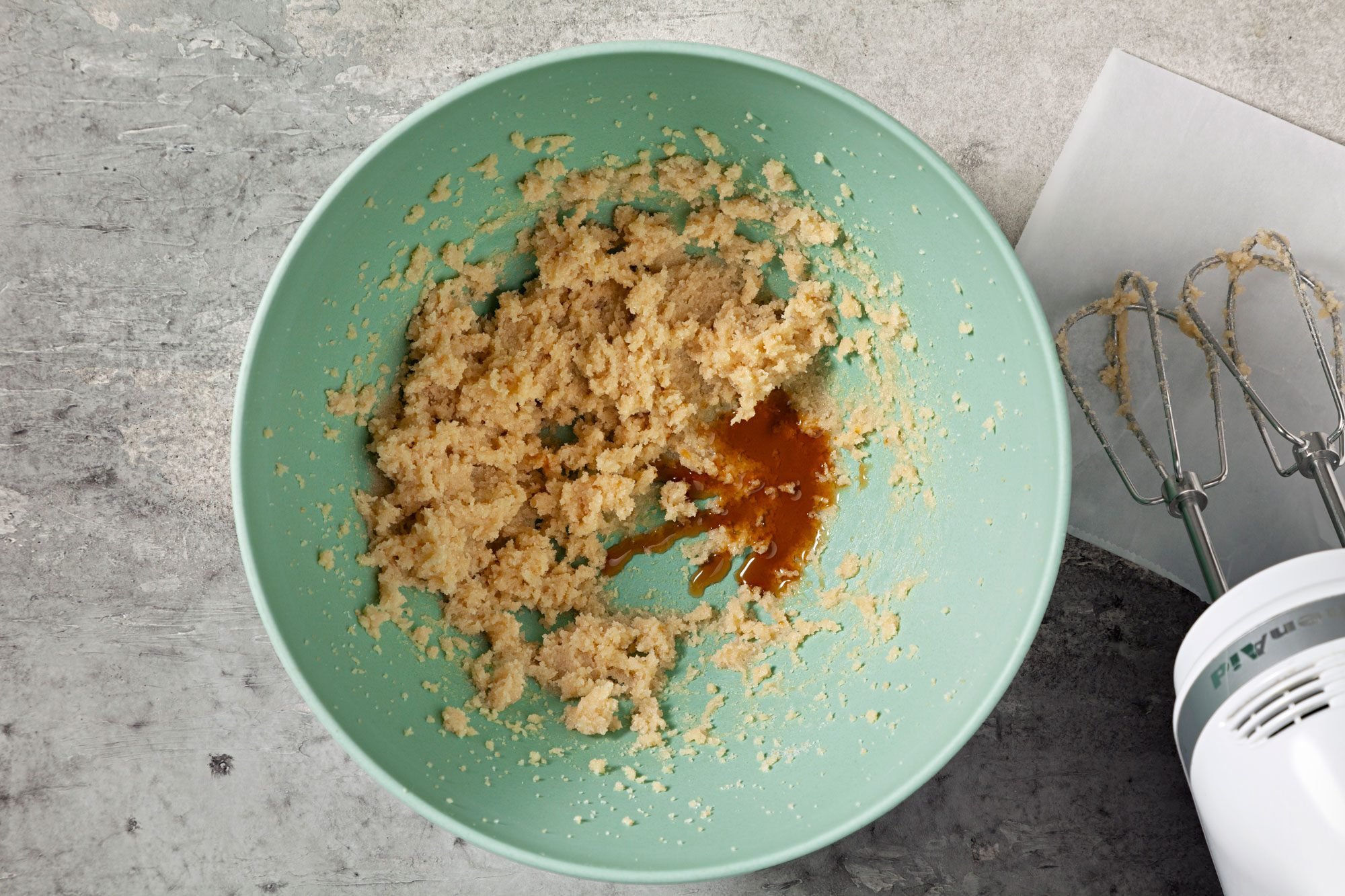 overhead shot; grey background; added vanilla essence in mixture in a large bowl; electric whisker;