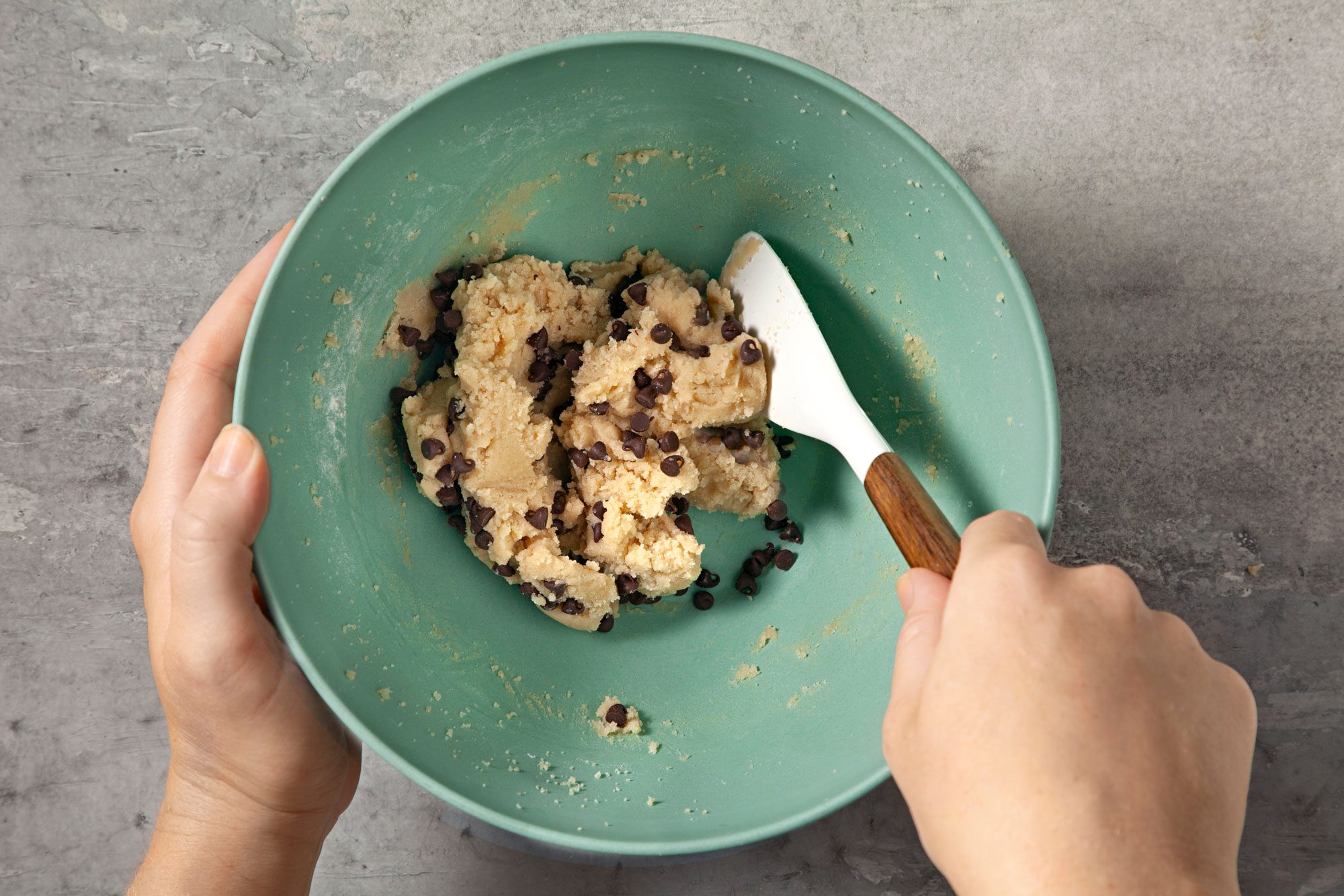 overhead shot; grey background; added chocolate chips into the mixture in the same bowl and mixing;