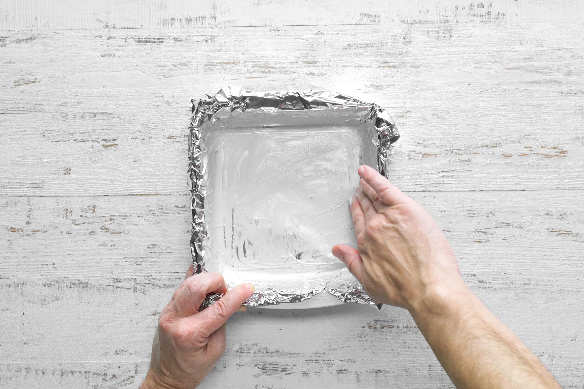 overhead shot; white wooden background; Lining an 8-in square pan with foil and butter the foil;