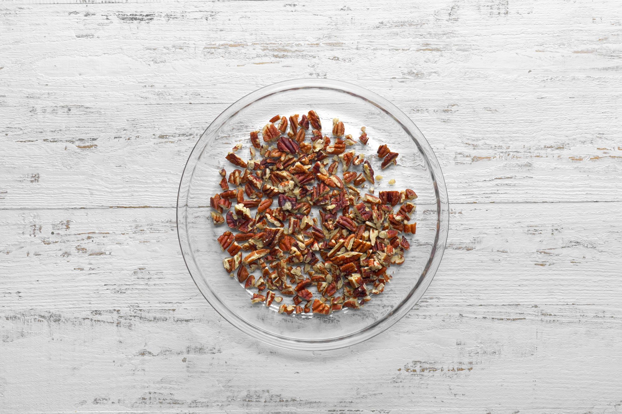 overhead shot; white wooden background; Placed pecans in a microwave-safe pie plate;