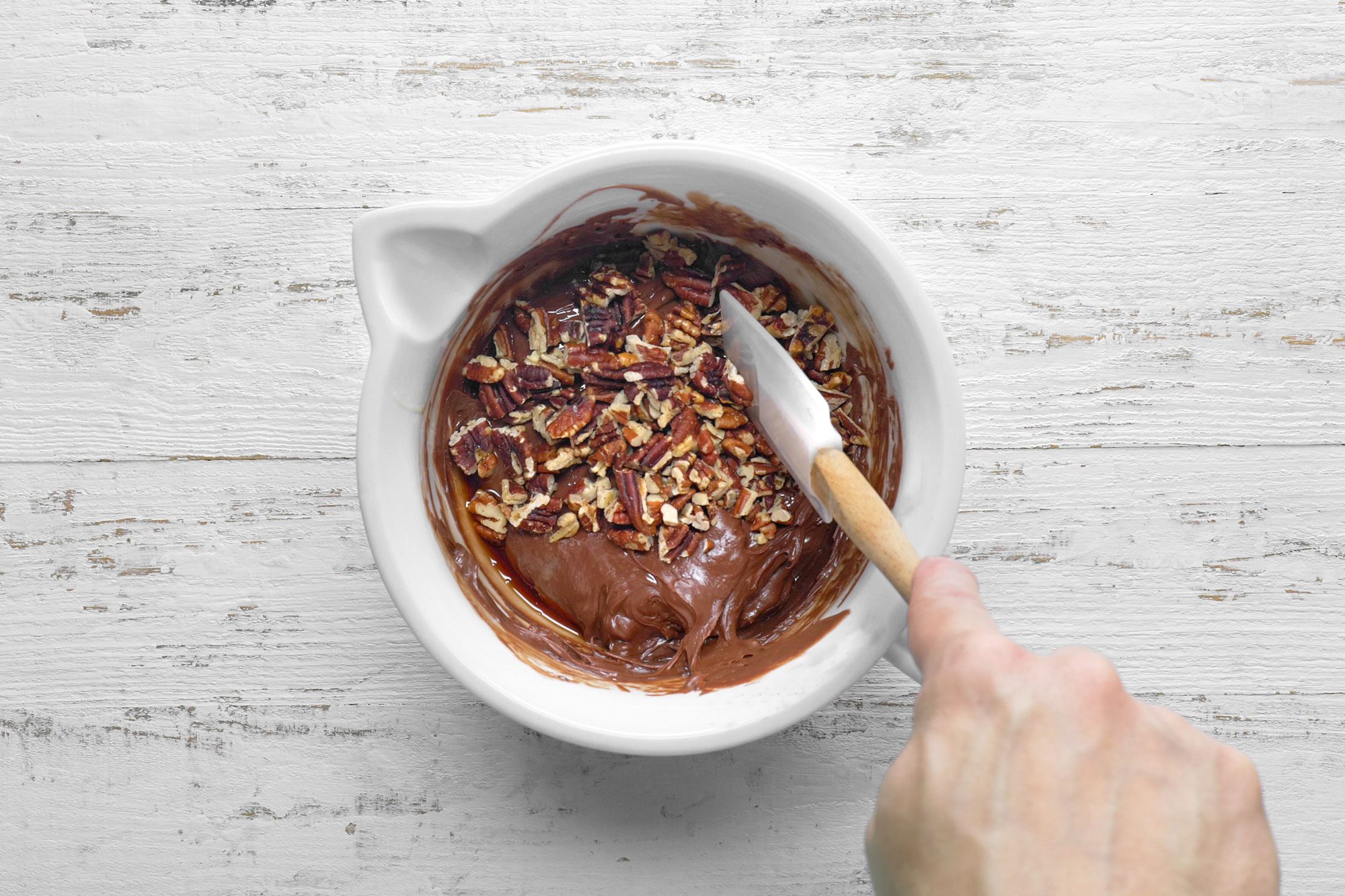 overhead shot; white wooden background; stiring the mixture with spatula;