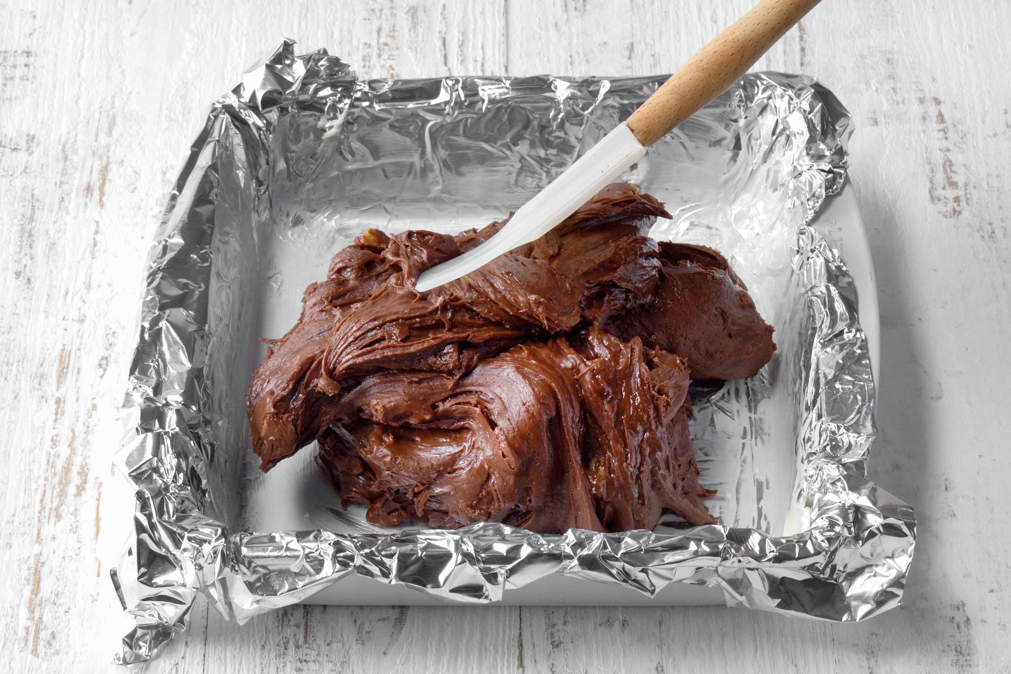 overhead shot; white wooden background; spreading mixture into the prepared pan;