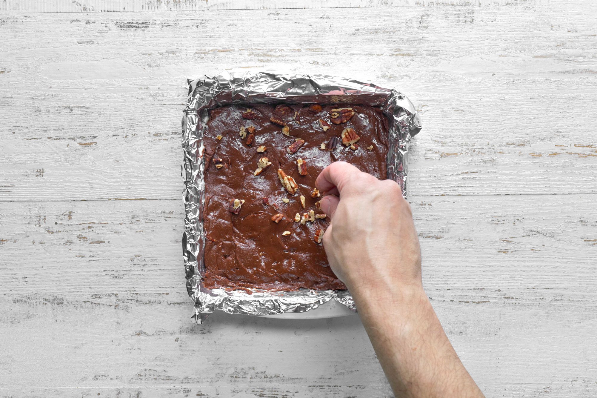 overhead shot; white wooden background; Sprinkling with remaining pecans over mixture;