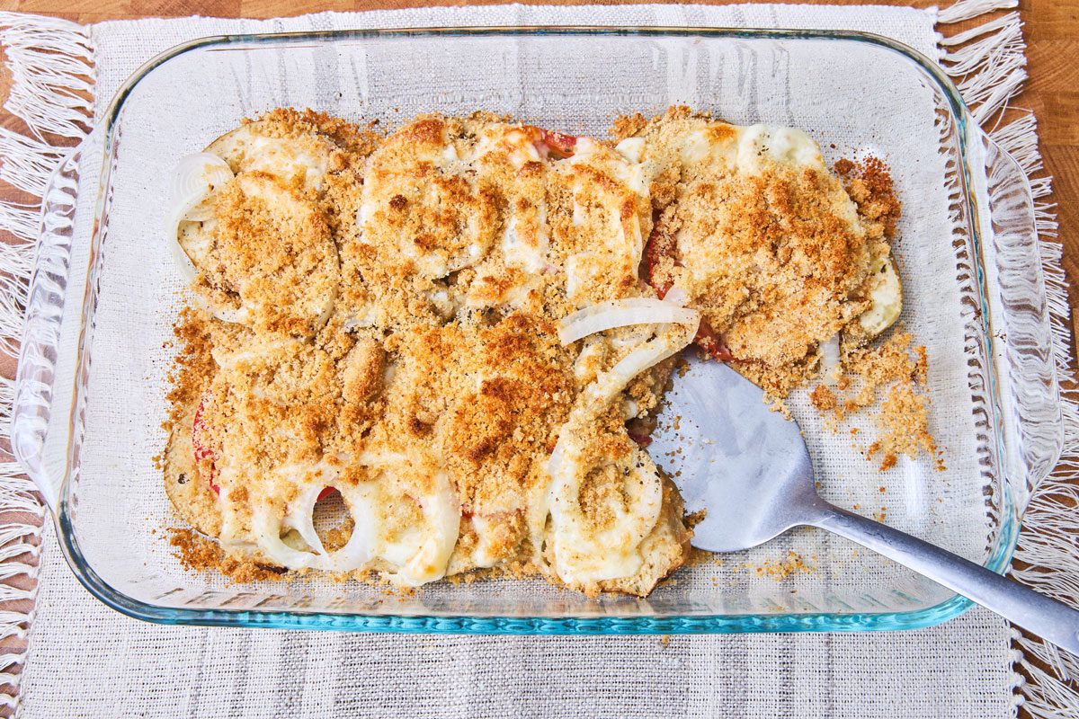 Baked eggplant casserole with melted cheese on top in dish with serving spoon