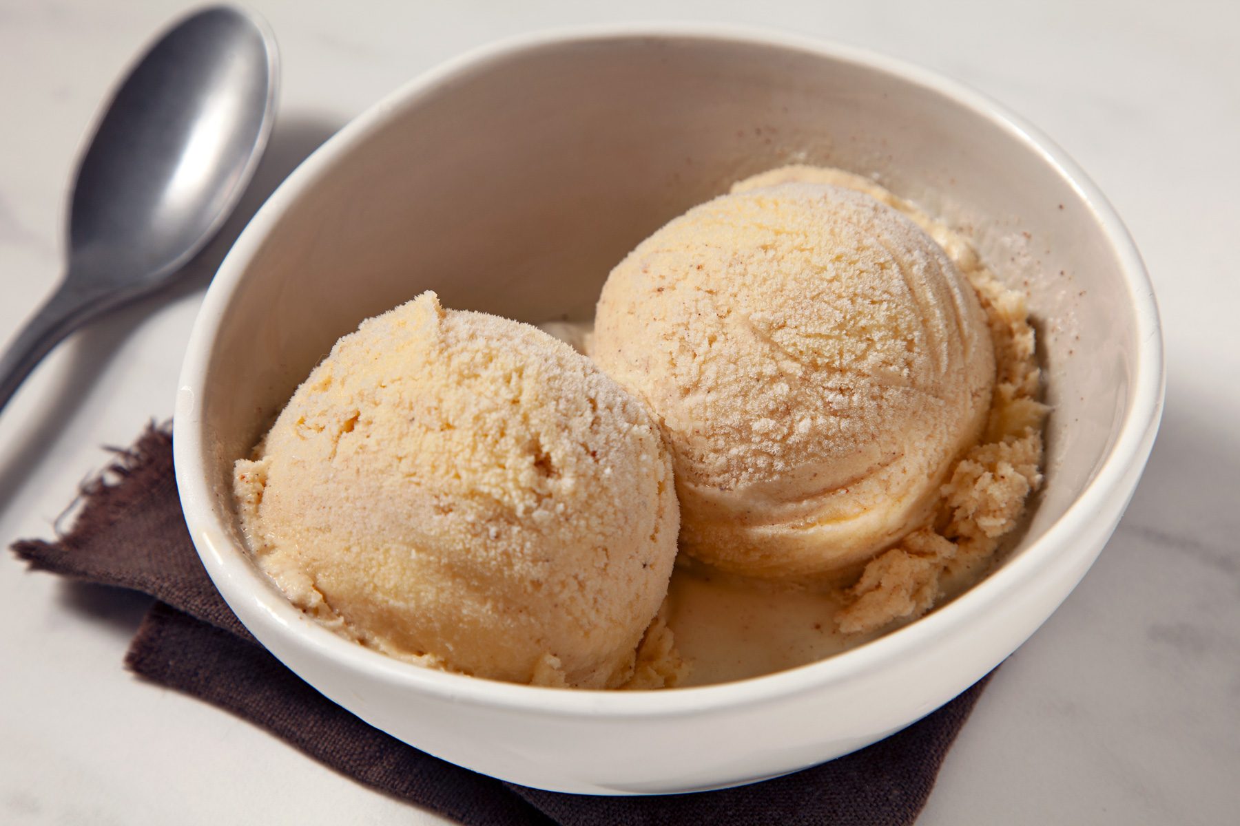 Eggnog Ice Cream scoops in a bowl with spoon on the side