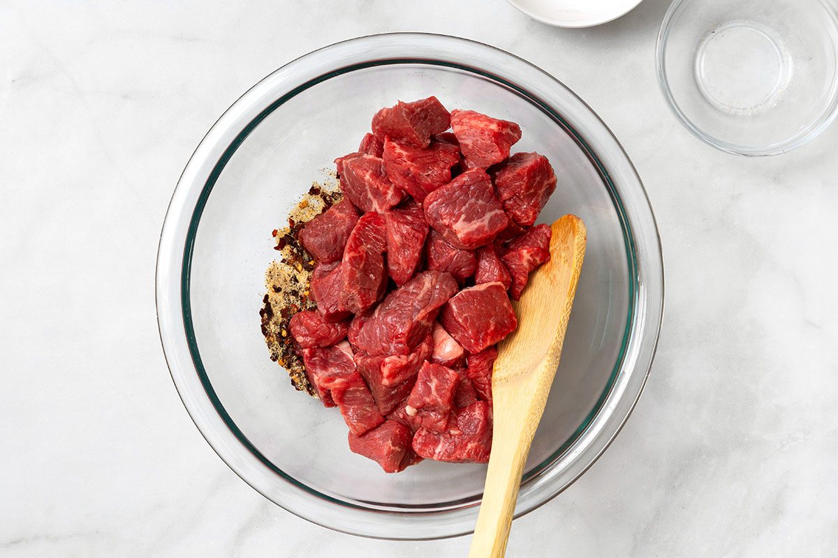 Bowl of cubed steak being mixed with seasonings for step one of Garlic Butter Steak Bite recipe for Taste of Home