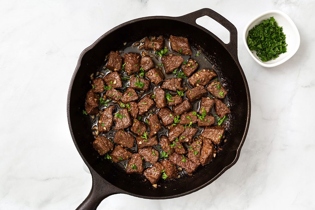 Large skillet of browned cubed steak with melted butter and garlic for step three of Garlic Butter Steak Bites