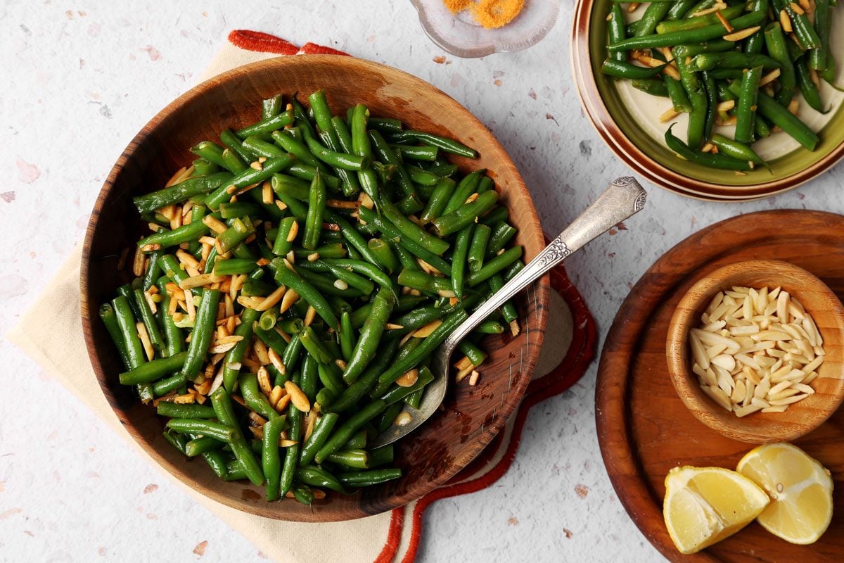 Taste of Home's Green Bean Almondine close up served in a wooden bowl on a white background.