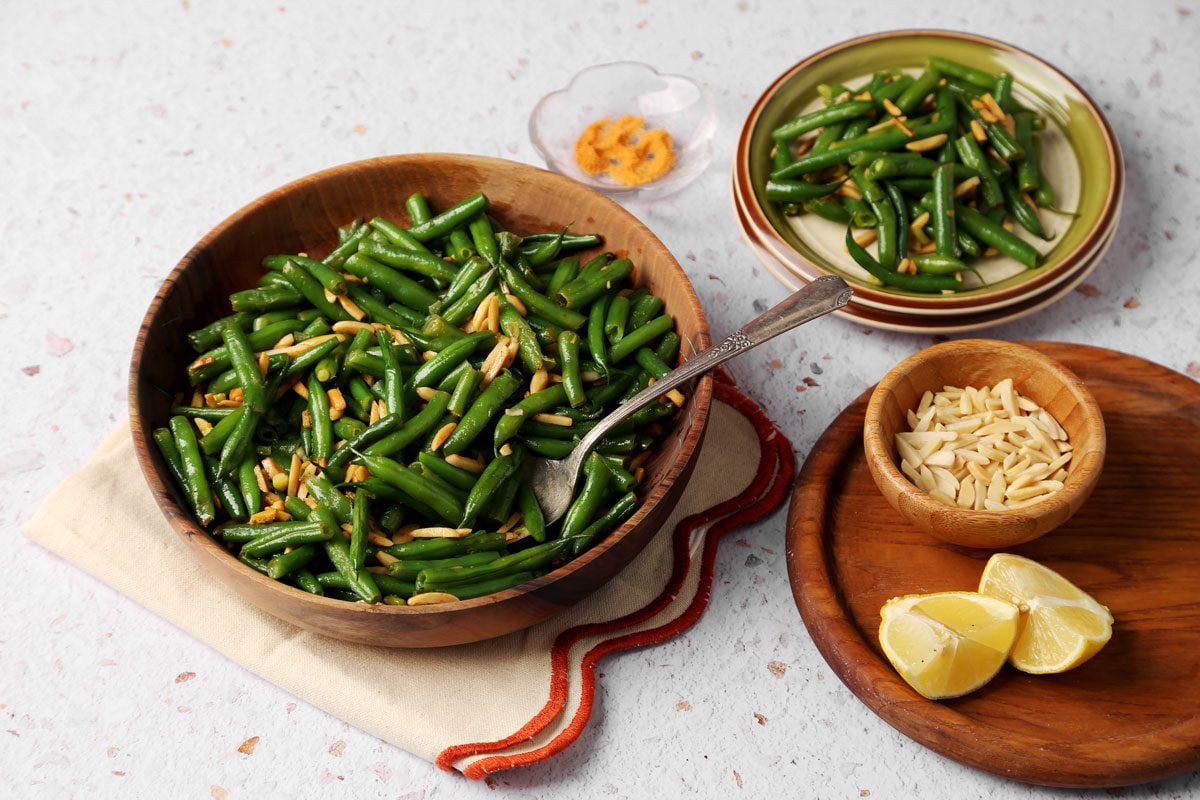 Taste of Home's Green Bean Almondine close up served in a wooden bowl on a white background.