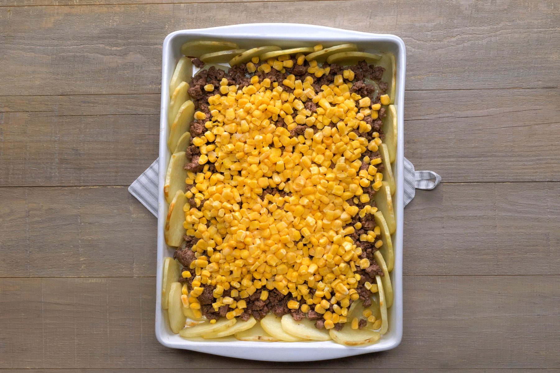 top shot of beef and corn sprinkled on potato slices in baking tray