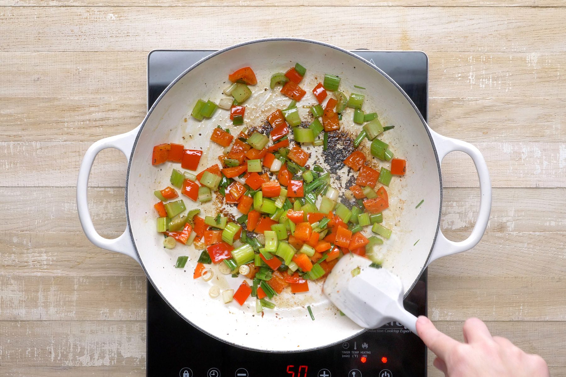 Top view shot of sautéing pepper, celery and onions in large skillet