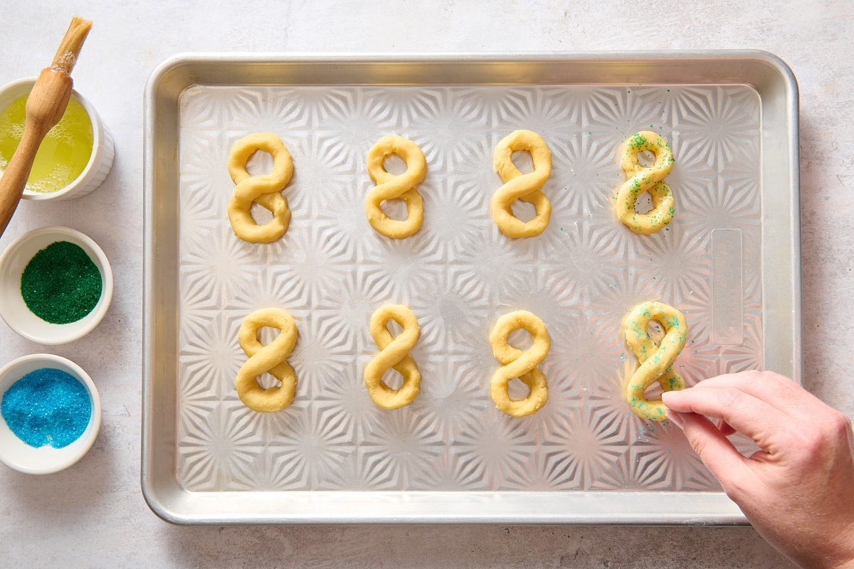 Sprinkling colored sugar over cookies on a baking sheet