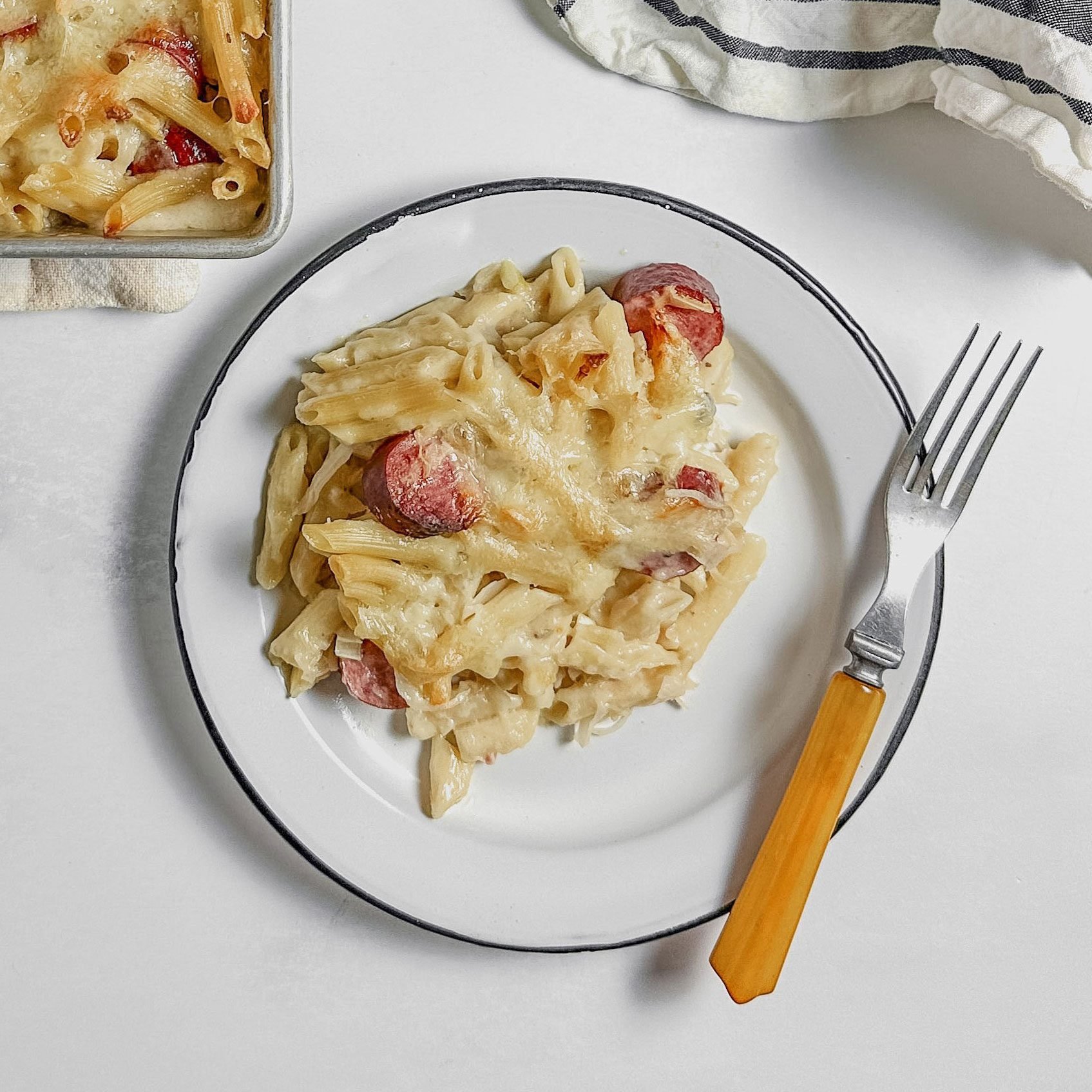 Taste of Home kielbasa casserole on an enamel plate next to a baking dish with kielbasa casserole.