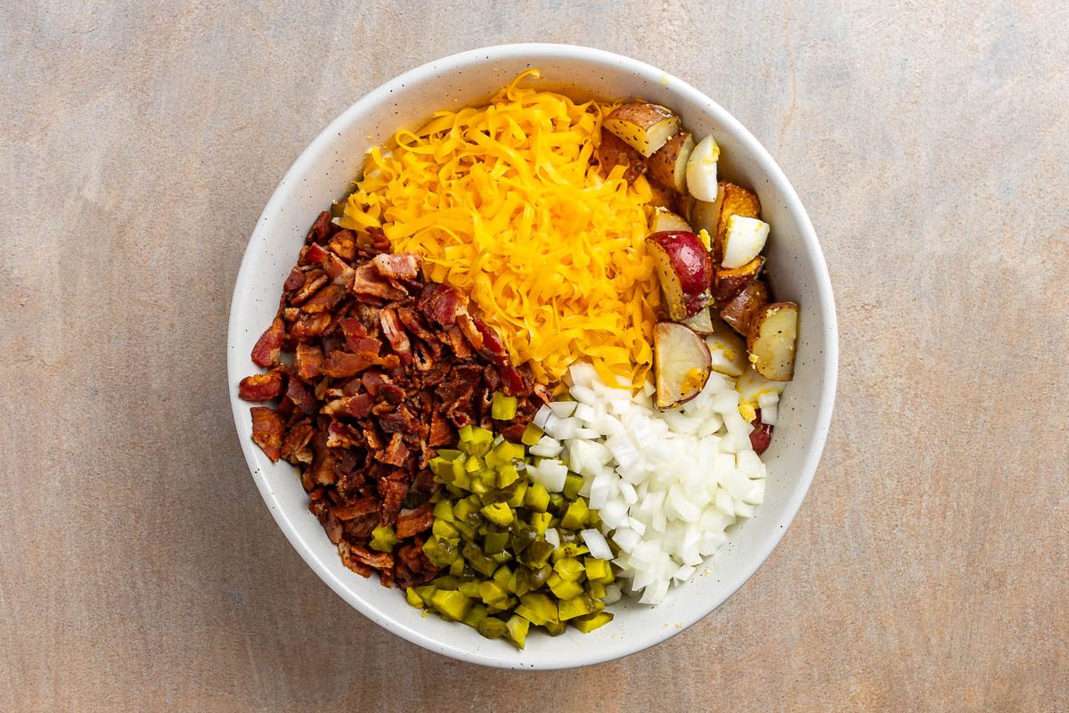 Taste of Home Loaded Baked Potato Salad recipe photo of the bacon, onion, cheese, and pickles added to the mixing bowl.