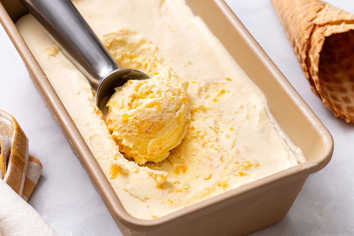 Orange ice cream in loaf pan with a scoop taken out