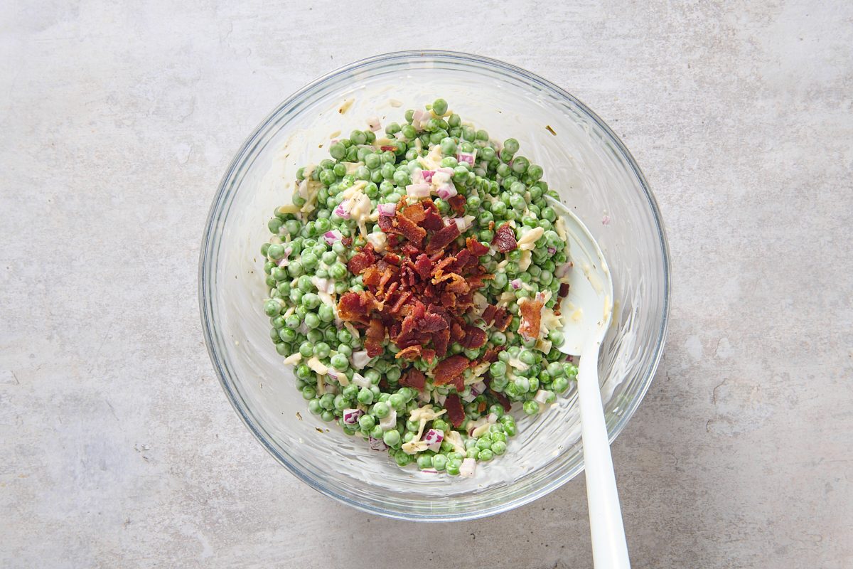 Stirring crumbled bacon into the chilled pea salad