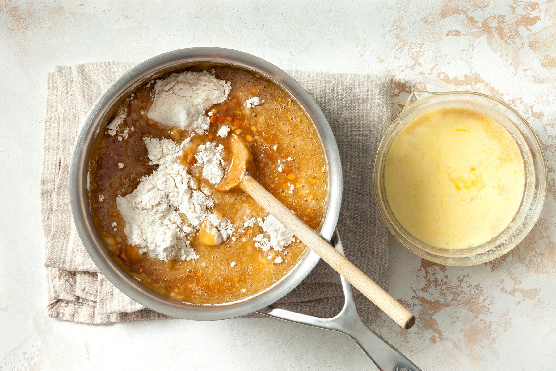 overhead shot; white textured background; in a saucepan, combined water and butter; mixed in peanut butter and oil until blended, Stir four mixture into peanut butter mixture, In a small bowl, whisked eggs, buttermilk and vanilla until blended; added flour to mixture;