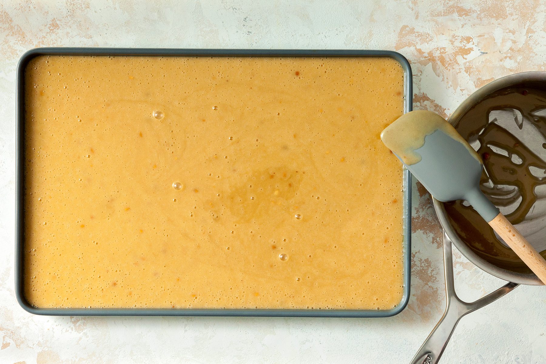 overhead shot; white textured background; Peanut Butter Sheet Cake batter transferred to a baking tray from a saucepan;