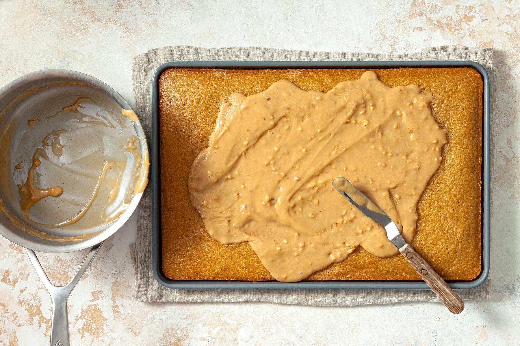 overhead shot; white textured background; Spooning glaze mixture over warm cake, spreading evenly with spreader;