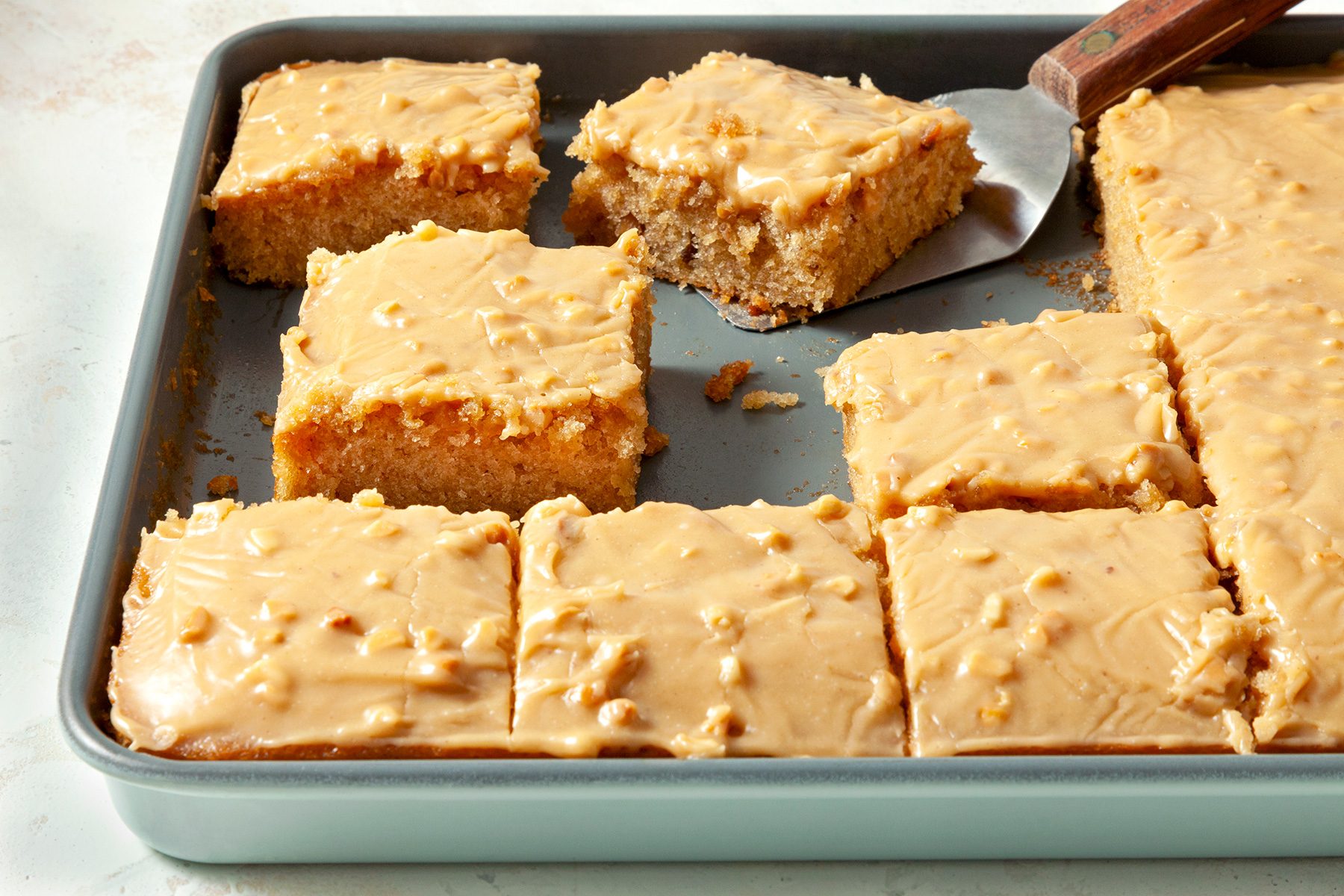 3/4th shot; horizontal; white textured background; Peanut Butter Sheet Cake cut into square pieces in baking tray;