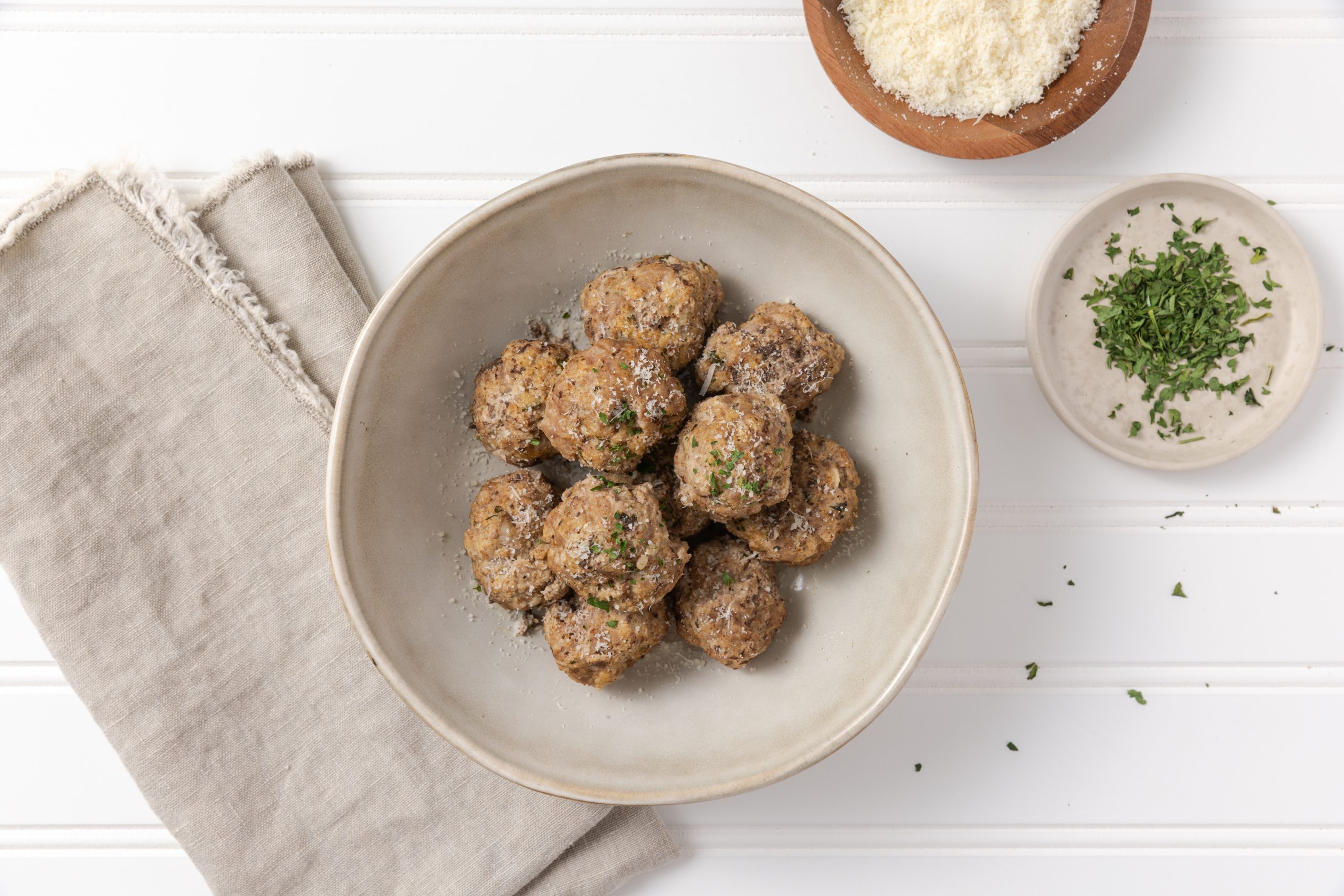 Meatballs served in bowl garnished with cheese and parsley.