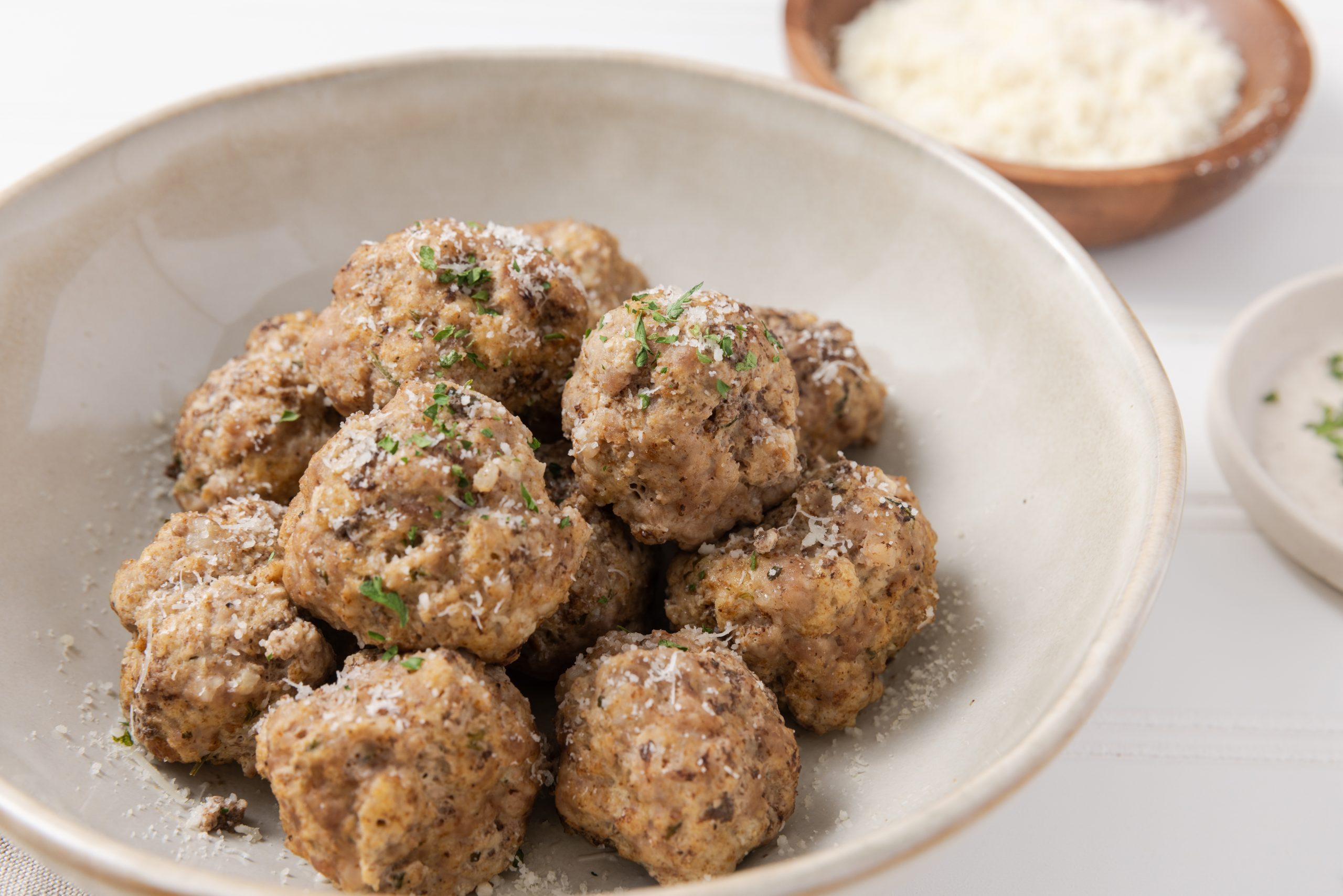 Meatballs served in bowl garnished with cheese and parsley.