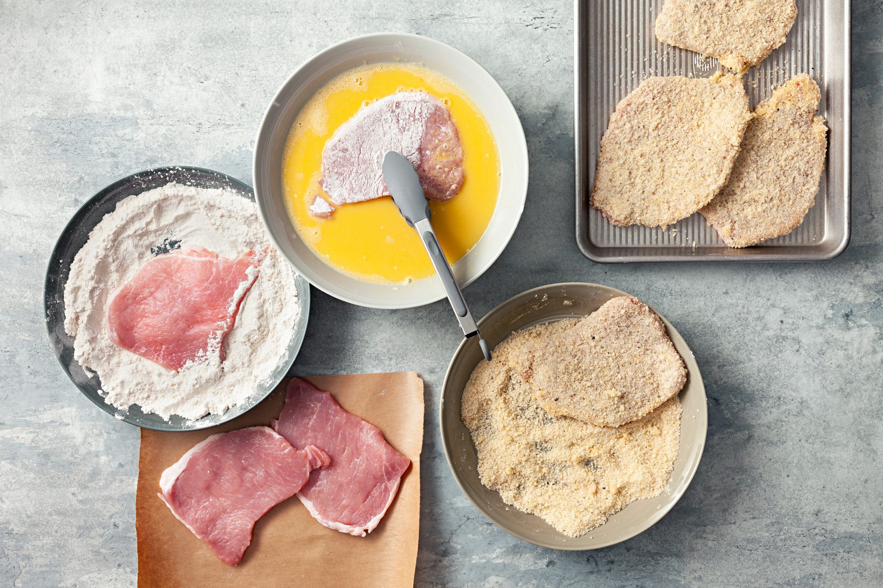 Top view shot of shallow bowl with bread crumbs, Parmesan, lemon zest, salt and pepper. Coating Pork with flour and egg