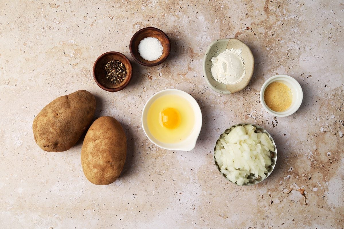 Ingredients laid out in various bowls for Taste Recipes's Potato Pancakes on a brown marble surface.