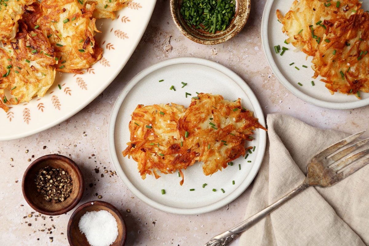 Close up of Taste of Home's Potato Pancakes served on plates with chives on a brown marble surface.