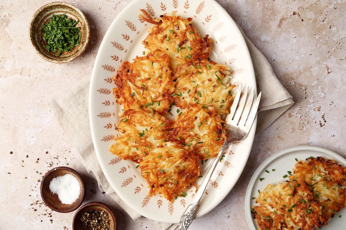 Close up of Taste Recipes's Potato Pancakes served on plates with chives on a brown marble surface.