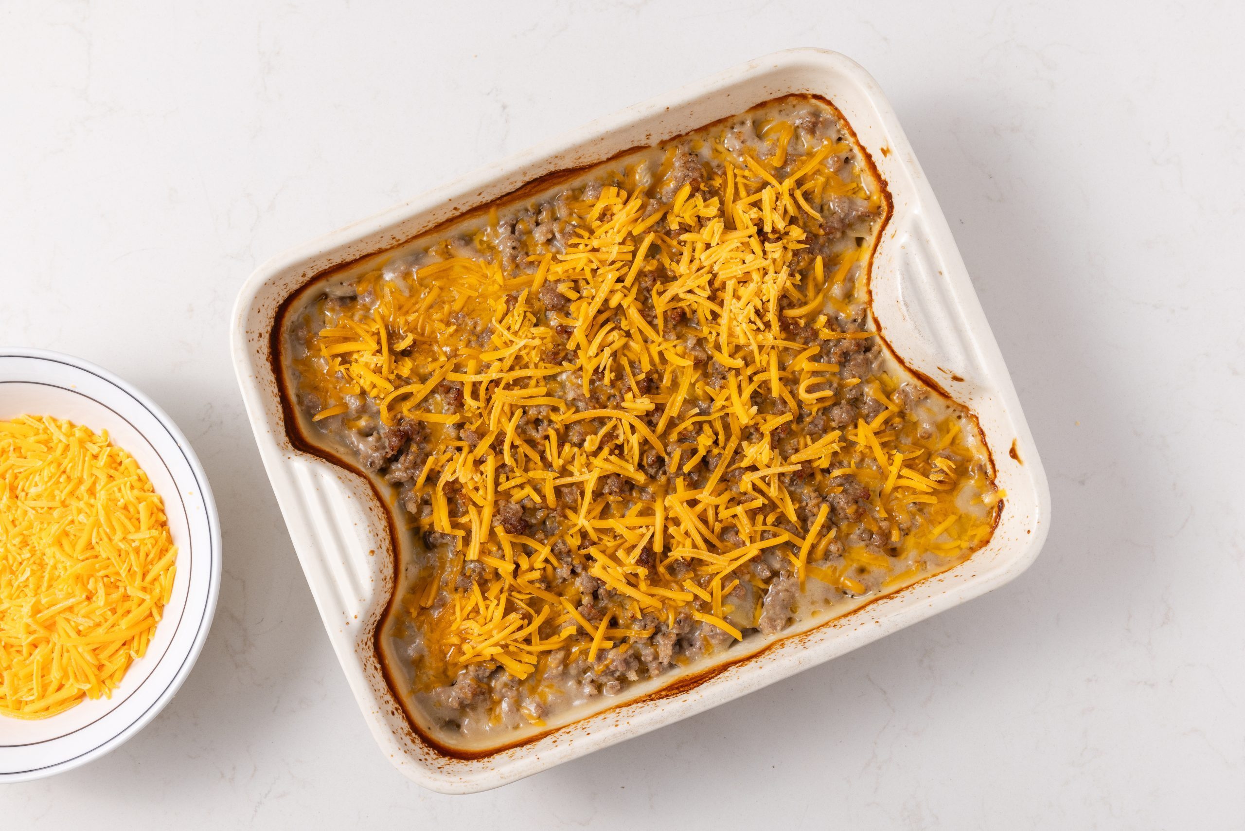 Casserole in baking dish topped with shredded cheddar cheese.