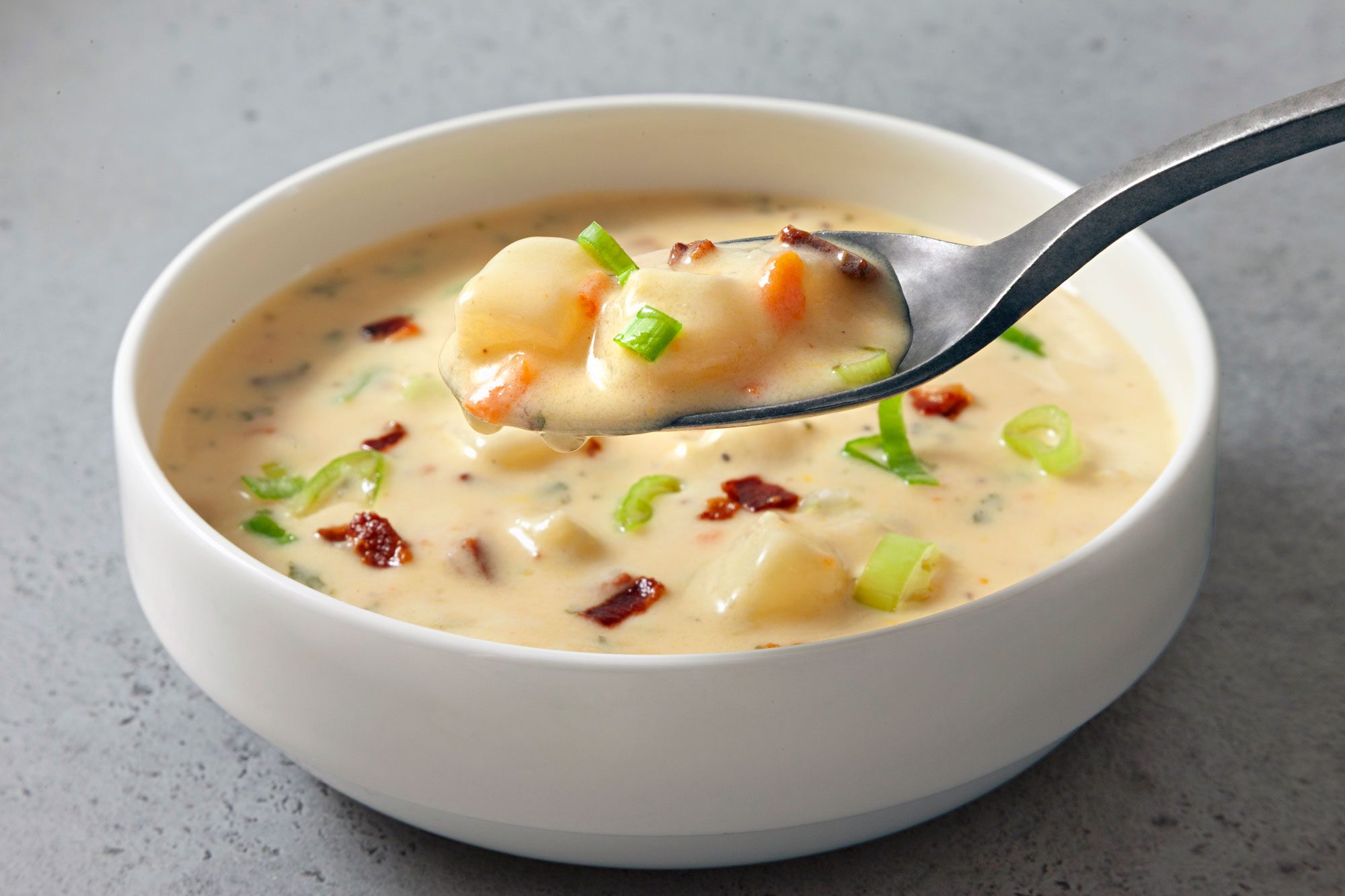 3/4th close shot; horizontal; light grey background; Potato Soup in small white bowl; a close view of Potato Soup in spoon;