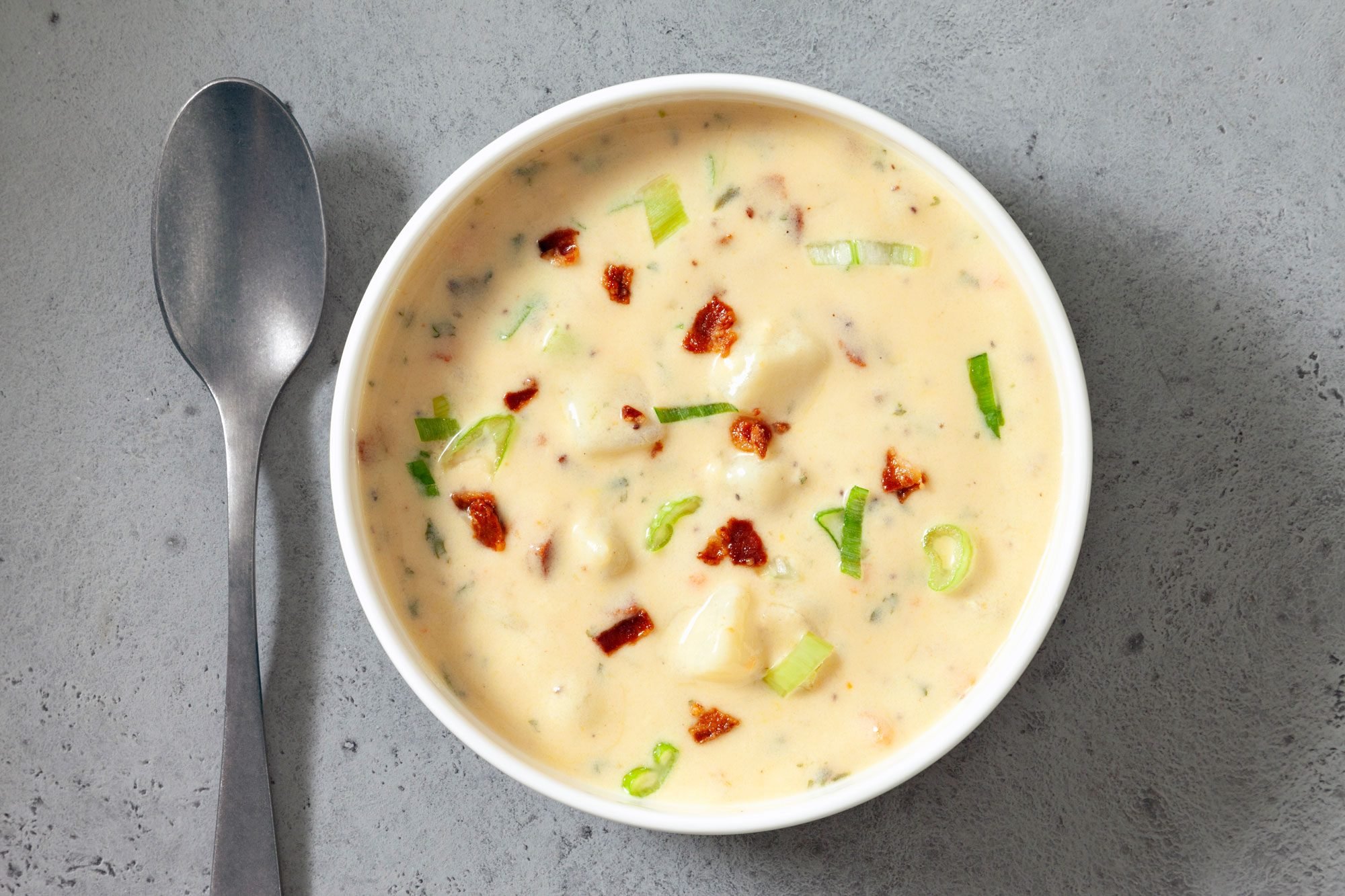 overhead shot; horizontal; light grey background; Potato Soup in small white bowl with silver spoon;