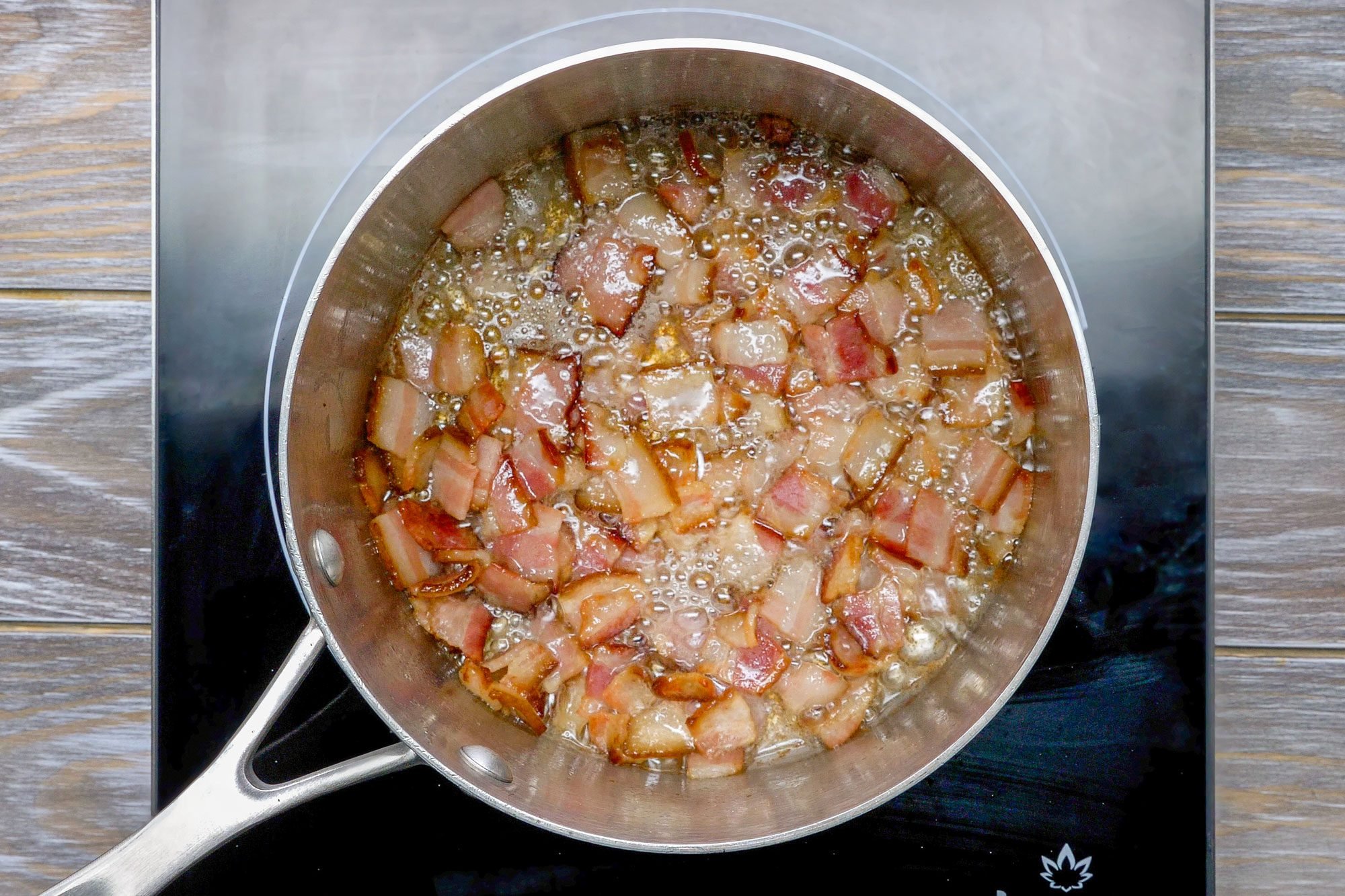 Overhead shot of a large saucepan; cook bacon over medium heat until crisp; induction; wooden background;