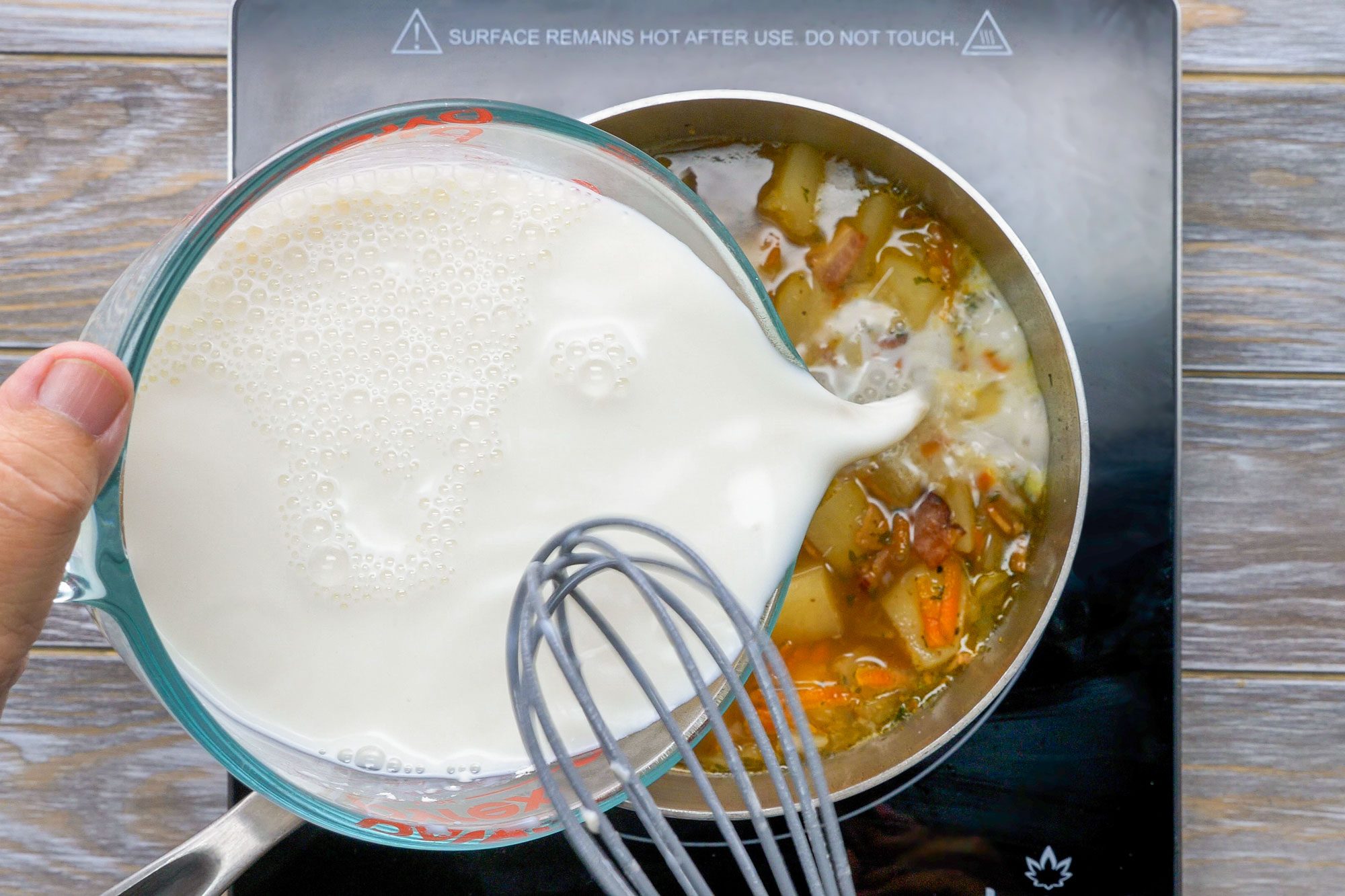 Overhead shot of a bowl; mix flour and milk until smooth; stir into soup; whisk tool; induction; wooden background;