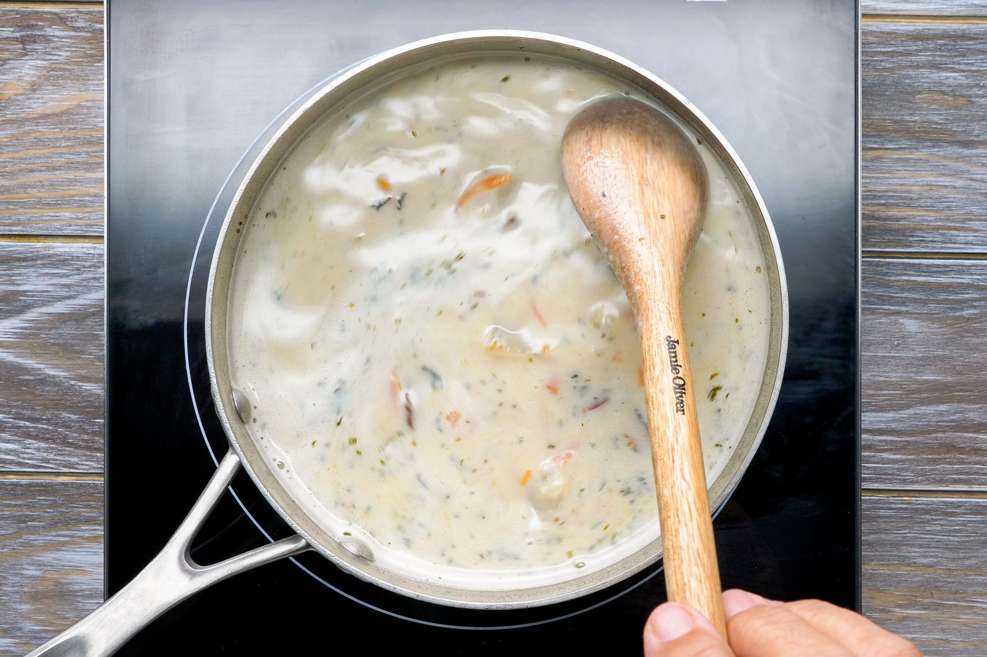 Overhead shot of soup; cook and stir until thickened; stir in cheese until melted; serve with green onions; wooden spoon; induction; wooden background;