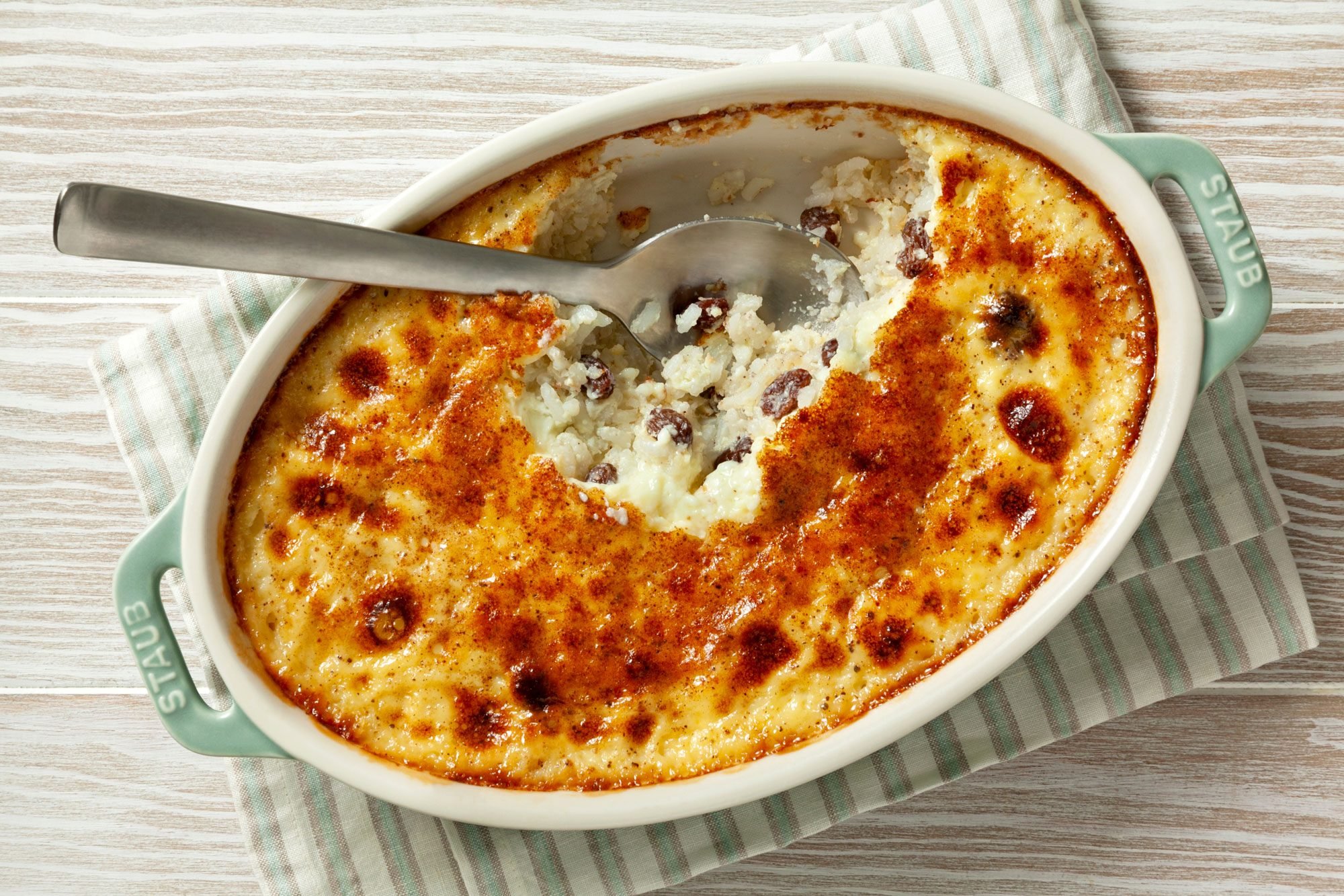 overhead shot; wooden background; Grandma's Rice Pudding in an oval dish over kitchen napkin with spoon;