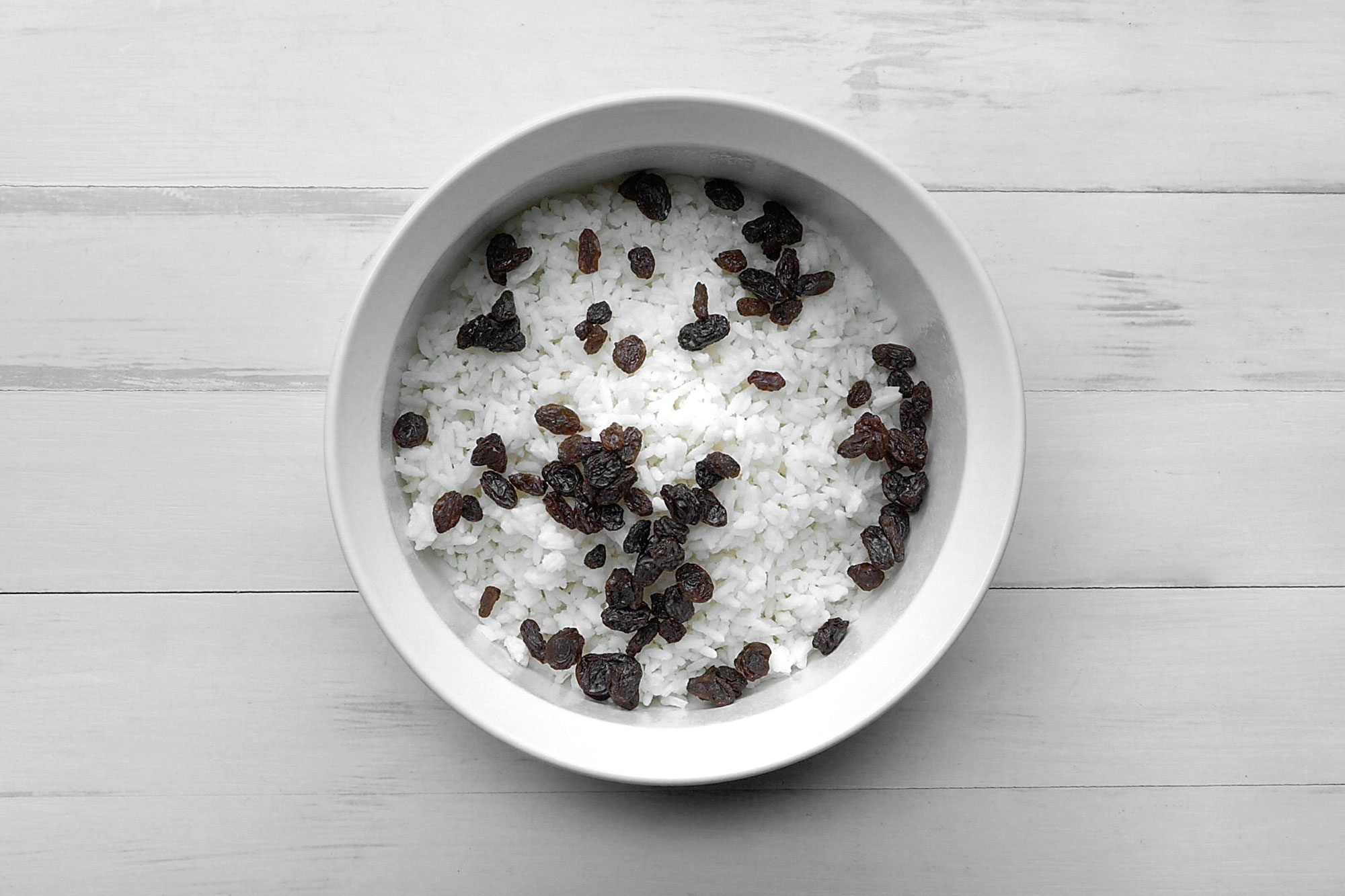 overhead shot; white background; Placed rice and raisins in a white greased casserole.