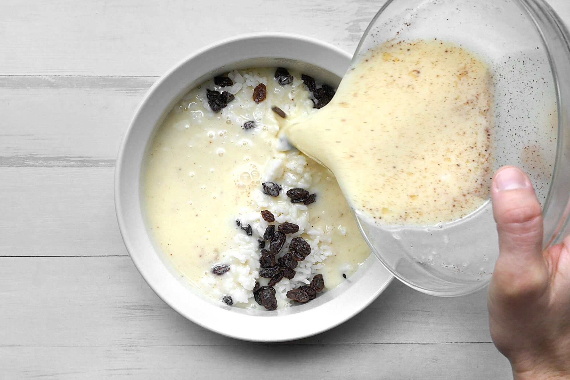 overhead shot; white background; pouring milk, egg, sugar mixture over rice;