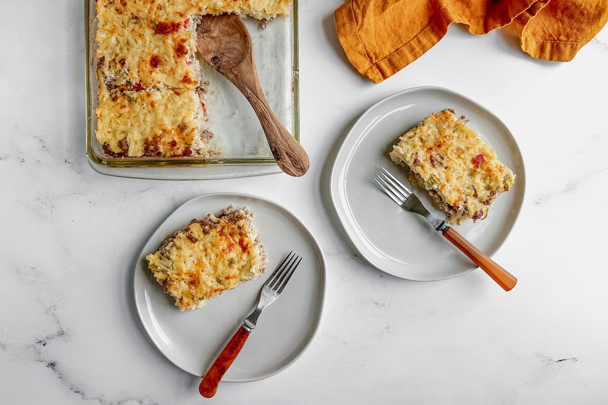 Taste of Home sausage hashbrown breakfast casserole on white plates on a marble surface.