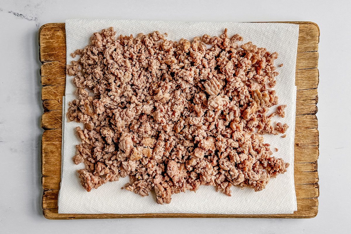 Cooked and drained sausage for Taste of Home Sausage Hashbrown Breakfast Casserole on paper towels on a wooden board on a marble surface.