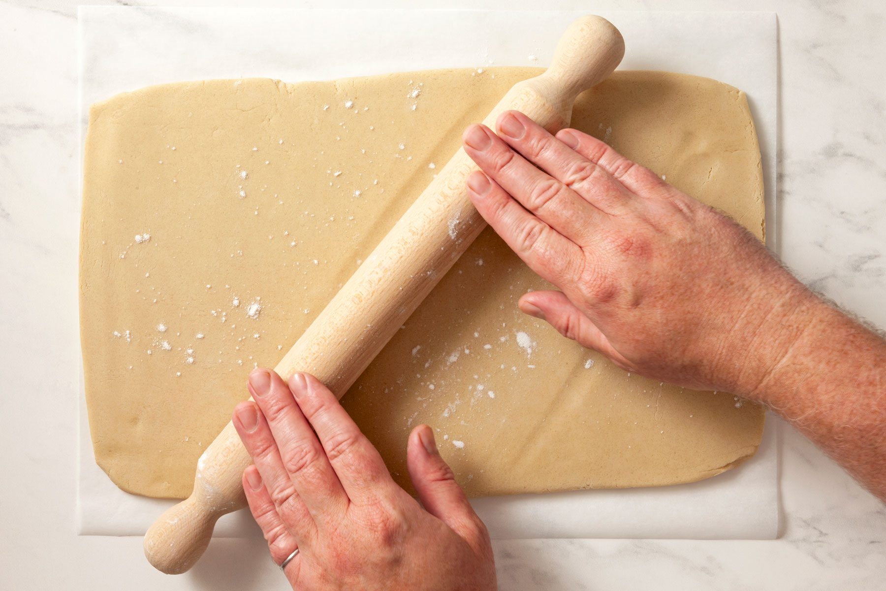 Hands can be seen rolling the dough on a baking parchment in the shape of a rectangle.